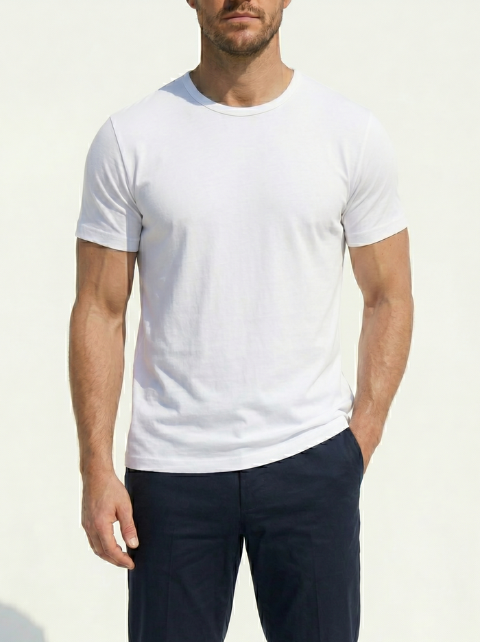 Man wearing a plain white t-shirt and dark pants on a light background
