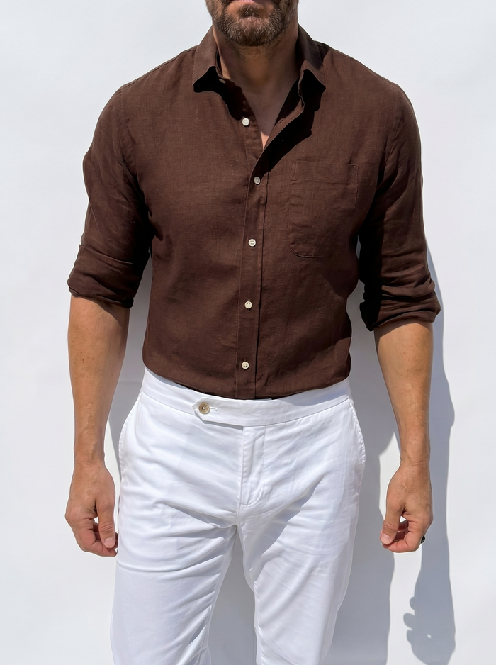 Man wearing a brown shirt and white pants against a light background