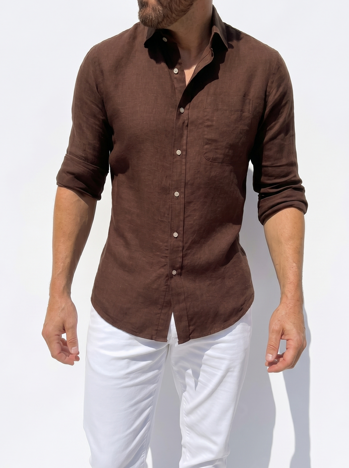 Man wearing a brown shirt with black collar and white pants on a light gray background