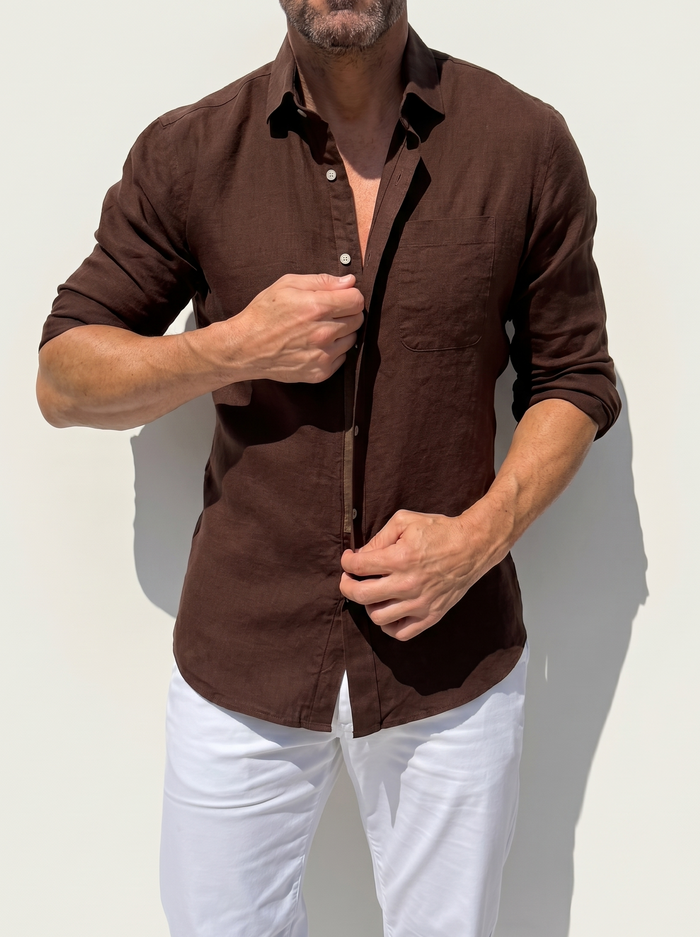 Man wearing a brown button-up shirt and white pants against a light background
