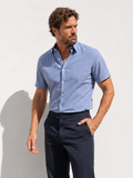 Man wearing a blue shirt and dark pants standing against a light background