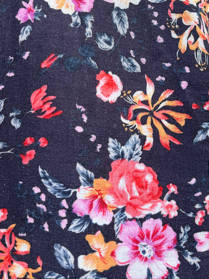 A close-up of a dark navy floral fabric with a vibrant print of pink, red, orange, and white flowers with green leaves.