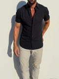 Man wearing a black short-sleeve shirt and light gray pants against a white background