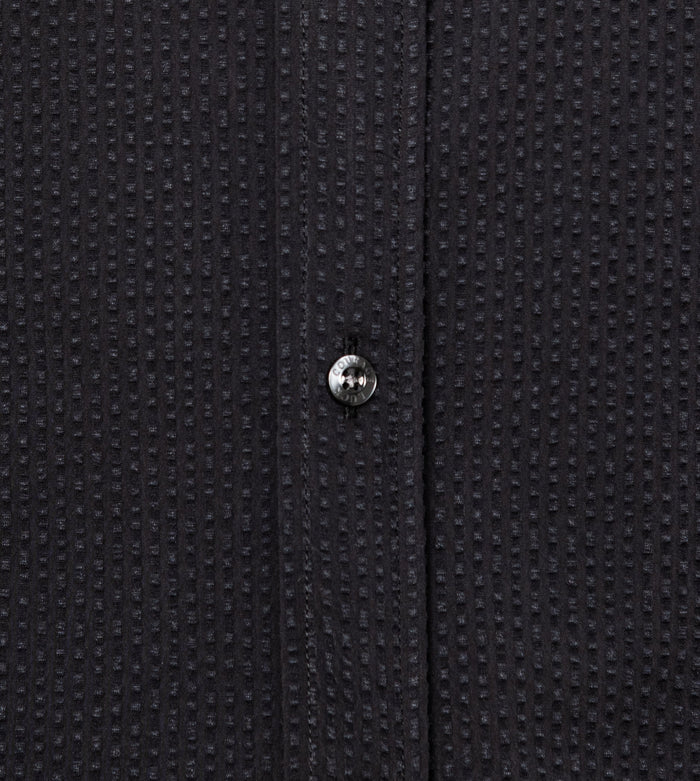Close-up of a textured black buttoned shirt with a button detail.