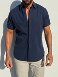 Man wearing a navy short-sleeve shirt and light gray pants against a white background