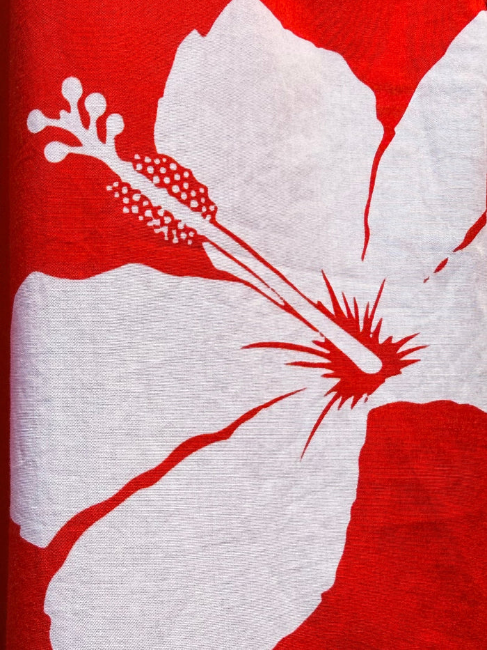 Close-up of a red Hawaiian-style shirt with a large white hibiscus flower print and a zipper detail.